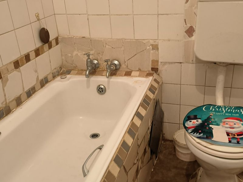 A dated bathroom featuring a bathtub and toilet with significant tile damage and wear, requiring renovation to restore functionality and aesthetic appeal.