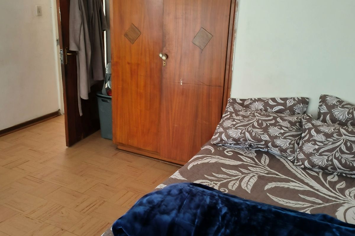 A bedroom featuring parquet flooring and a built-in wooden wardrobe, requiring cosmetic updates to improve the overall aesthetic.