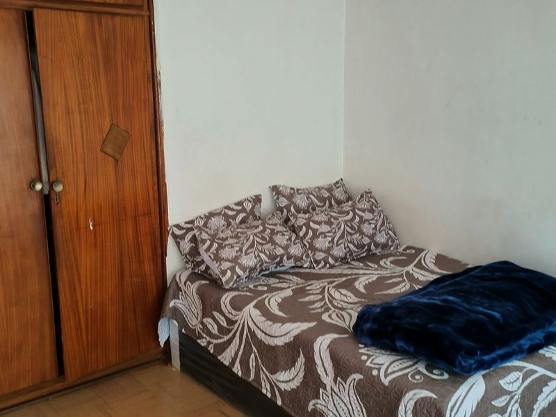 A bedroom featuring a built-in wooden wardrobe and parquet flooring, offering a functional space in need of cosmetic updates.