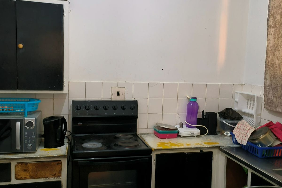 A dated kitchen area featuring built-in cabinetry, an electric stove, and a tiled backsplash, currently requiring cosmetic updates and refurbishment.