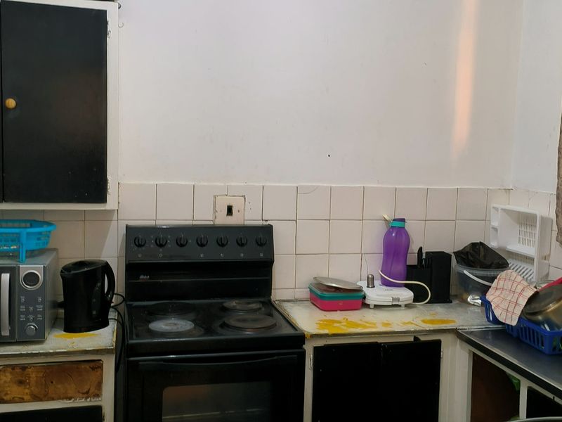 A dated kitchen area featuring built-in cabinetry, an electric stove, and a tiled backsplash, currently requiring cosmetic updates and refurbishment.