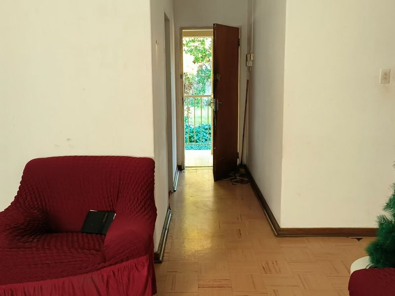 Living area featuring parquet flooring and direct access to an exterior entrance, showing signs of wear on walls and floors.