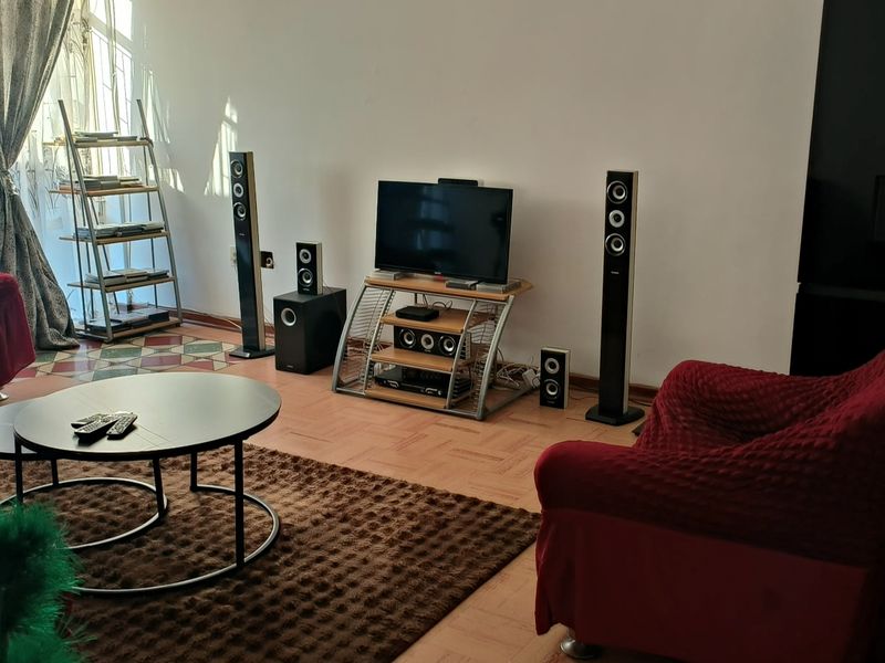 A living room featuring parquet flooring and a large window, providing a functional space for relaxation.