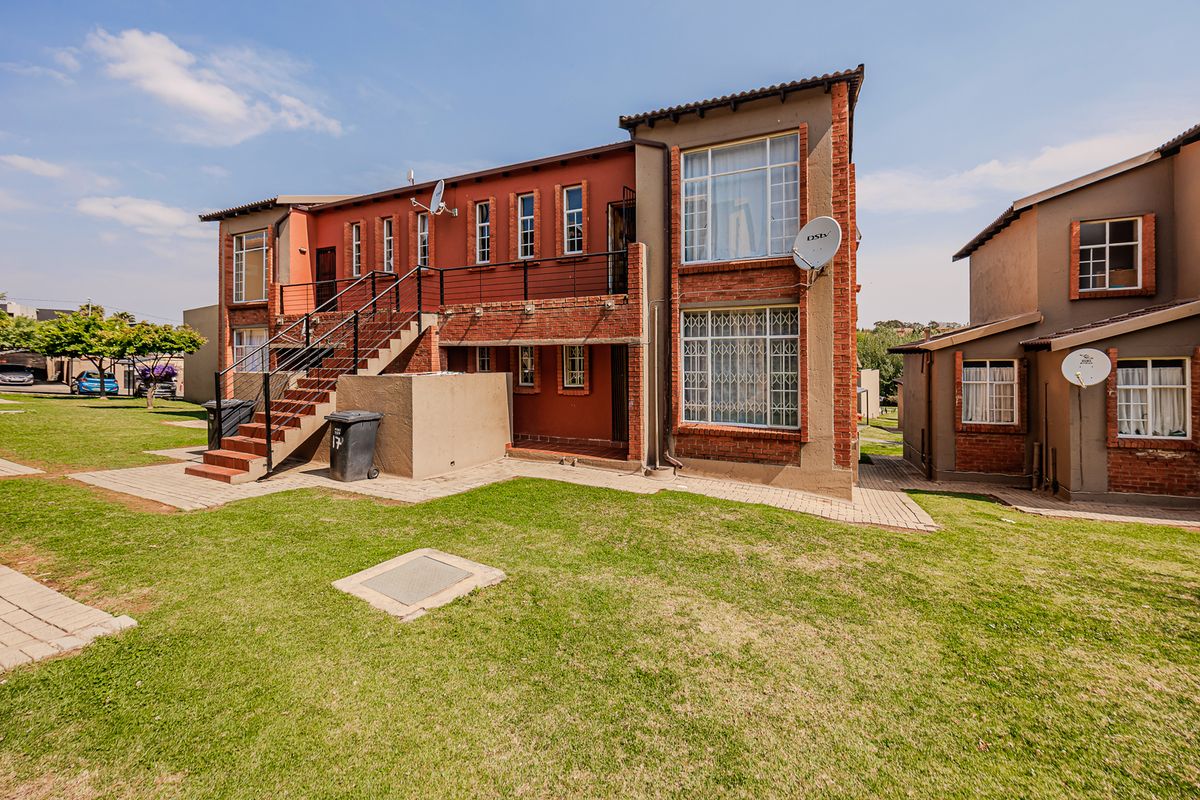 Rear view of a multi-story apartment building featuring brick construction, an external staircase with metal railings, and surrounding communal lawn areas.