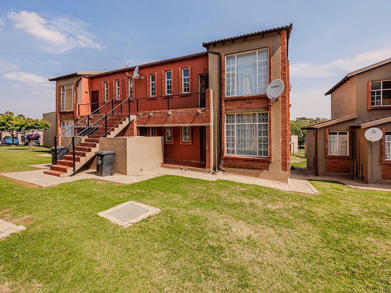 Rear view of a multi-story apartment building featuring brick construction, an external staircase with metal railings, and surrounding communal lawn areas.