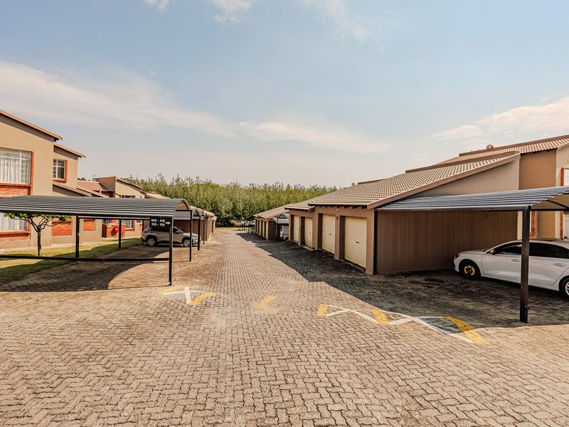 Exterior view of an apartment complex featuring a paved driveway, multiple carport structures, and a row of garages with tiled roofing.