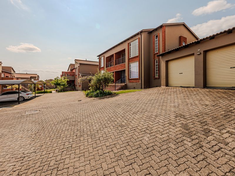 Exterior view of an apartment complex featuring a paved driveway, double garage with roller doors, and covered parking bays.