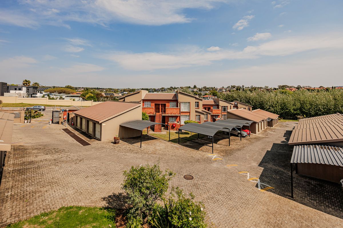Aerial view of an apartment complex featuring paved driveways, covered parking carports, and multi-story brick residential buildings.