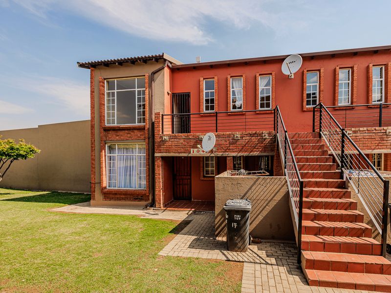 Rear view of a multi-story apartment building featuring a brick facade, external staircase with metal railings, and a paved walkway leading to the entrance.