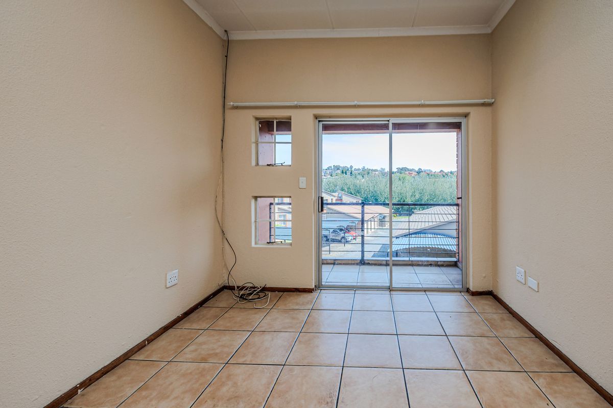 An empty living area featuring tiled flooring and a sliding glass door providing access to a balcony with neighborhood views.