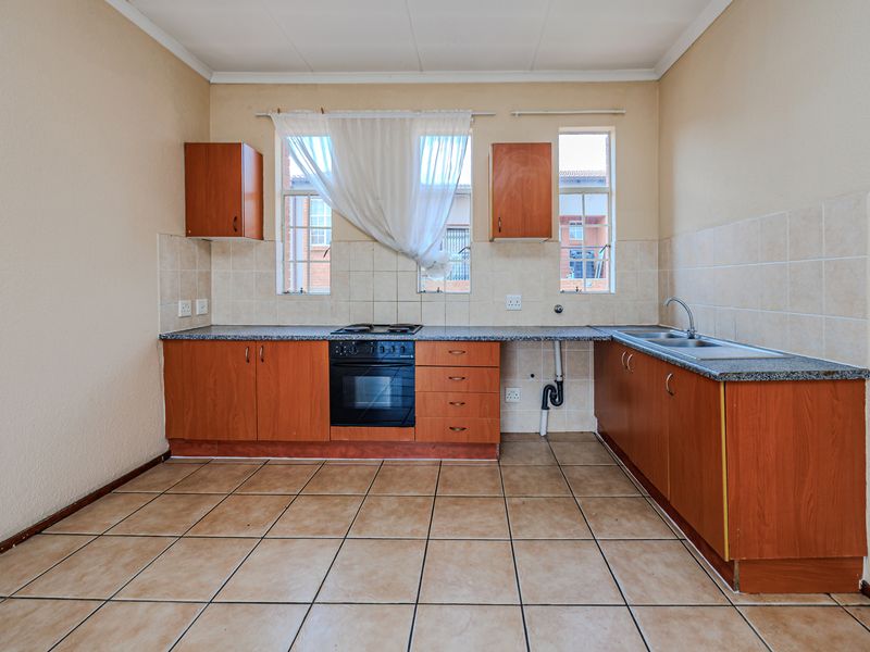A functional, empty kitchen featuring wood-finish cabinetry, laminate countertops, a built-in oven with hob, and tiled flooring throughout.