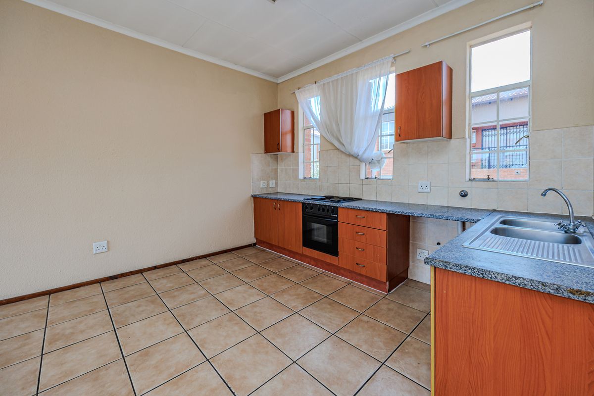 A functional, empty kitchen featuring wooden cabinetry, laminate countertops, a built-in oven, hob, and a stainless steel sink with tiled flooring and backsplash.