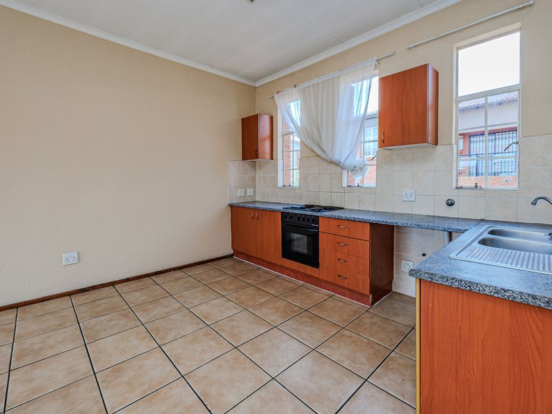 A functional, empty kitchen featuring wooden cabinetry, laminate countertops, a built-in oven, hob, and a stainless steel sink with tiled flooring and backsplash.
