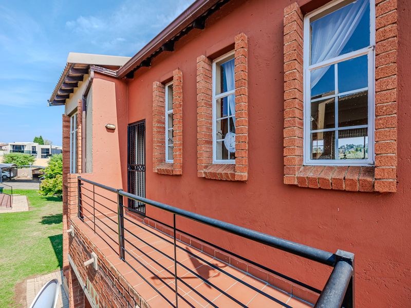 A private balcony featuring tiled flooring, a secure metal balustrade, and classic brick-framed windows overlooking the surrounding apartment complex grounds.