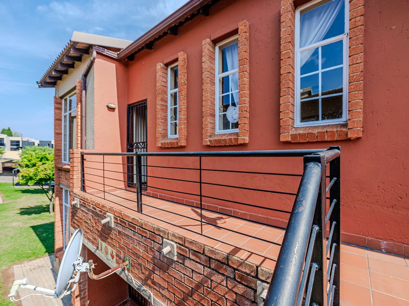 An elevated balcony featuring tiled flooring, a metal balustrade, and brick exterior detailing, providing an outdoor space accessible via a security gate.