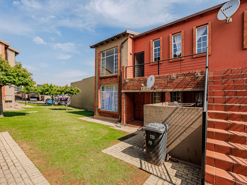 Rear view of a multi-story apartment building featuring a brick facade, tiled staircase, and a balcony overlooking a communal garden area.