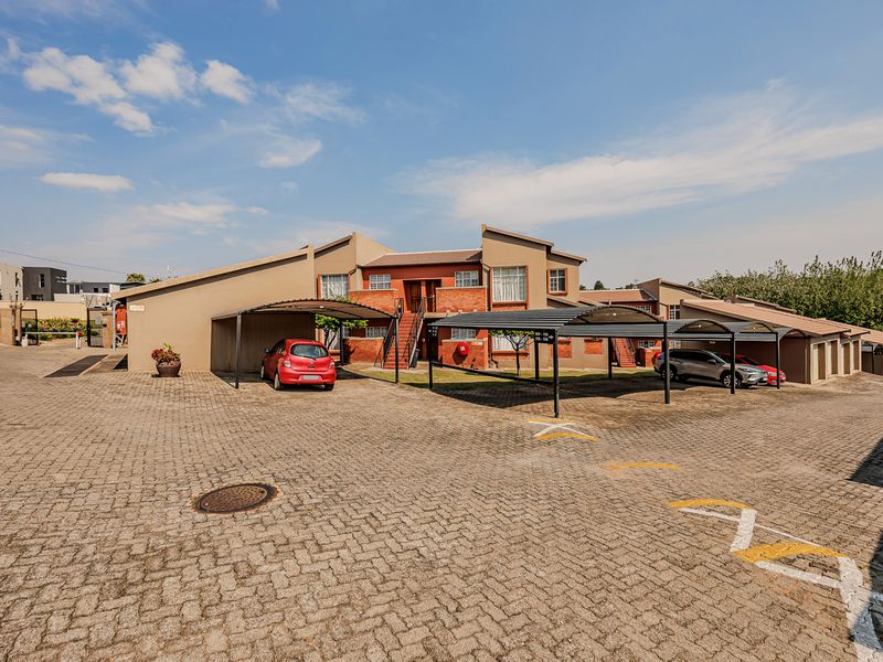 Exterior view of an apartment complex featuring a paved parking area with covered carports and brick building facades.