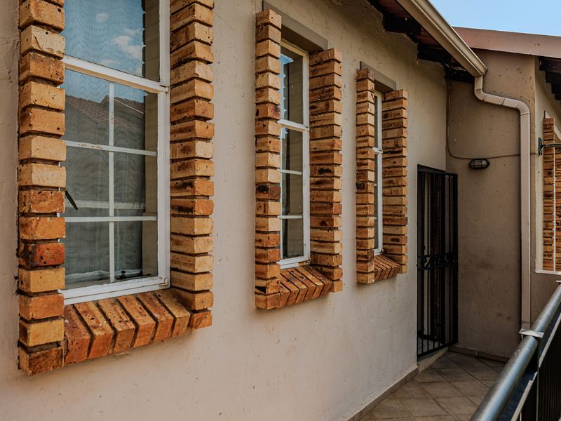 A balcony area featuring brick-detailed window surrounds, tiled flooring, and a metal security gate, providing access to the exterior of the apartment.