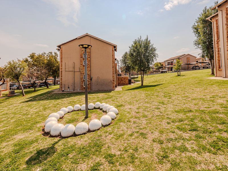 A view of the communal garden area between apartment blocks, featuring brick facades, manicured lawn, and exterior lighting.
