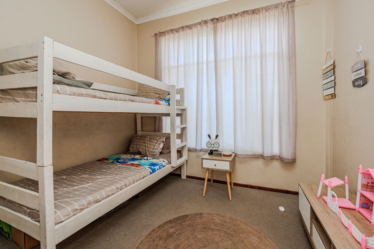 A functional bedroom featuring carpeted flooring and a large window with sheer curtains, providing natural light.