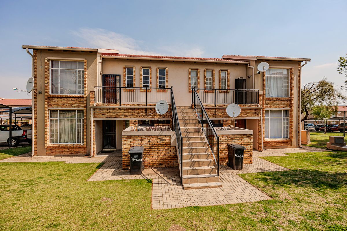 Rear view of a two-story apartment building featuring brick facade, external staircase, paved walkways, and communal garden space.