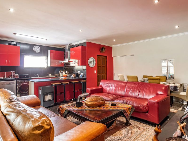 Open-plan living and kitchen area featuring high-gloss red cabinetry, subway tile backsplash, and recessed lighting, with visible ceiling water staining.