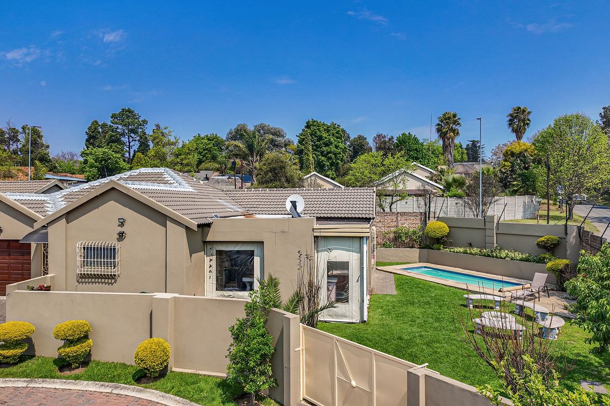 Aerial view of a residential property featuring a swimming pool, landscaped garden, paved driveway, and secure boundary walls.