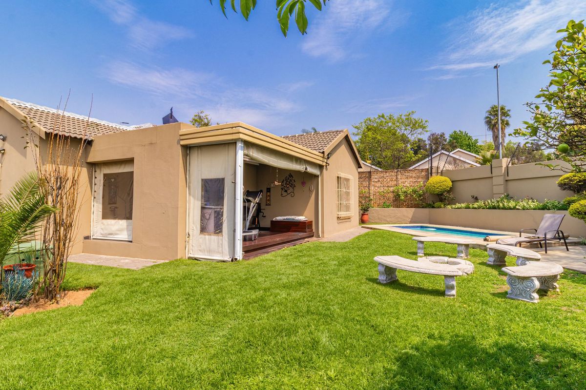 Rear garden view featuring a swimming pool, paved surround, and a covered patio area with roll-down blinds attached to the main house structure.