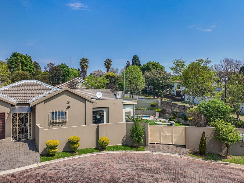 An elevated view of the property's front facade, featuring a paved driveway, secure garage, and well-maintained boundary walls.