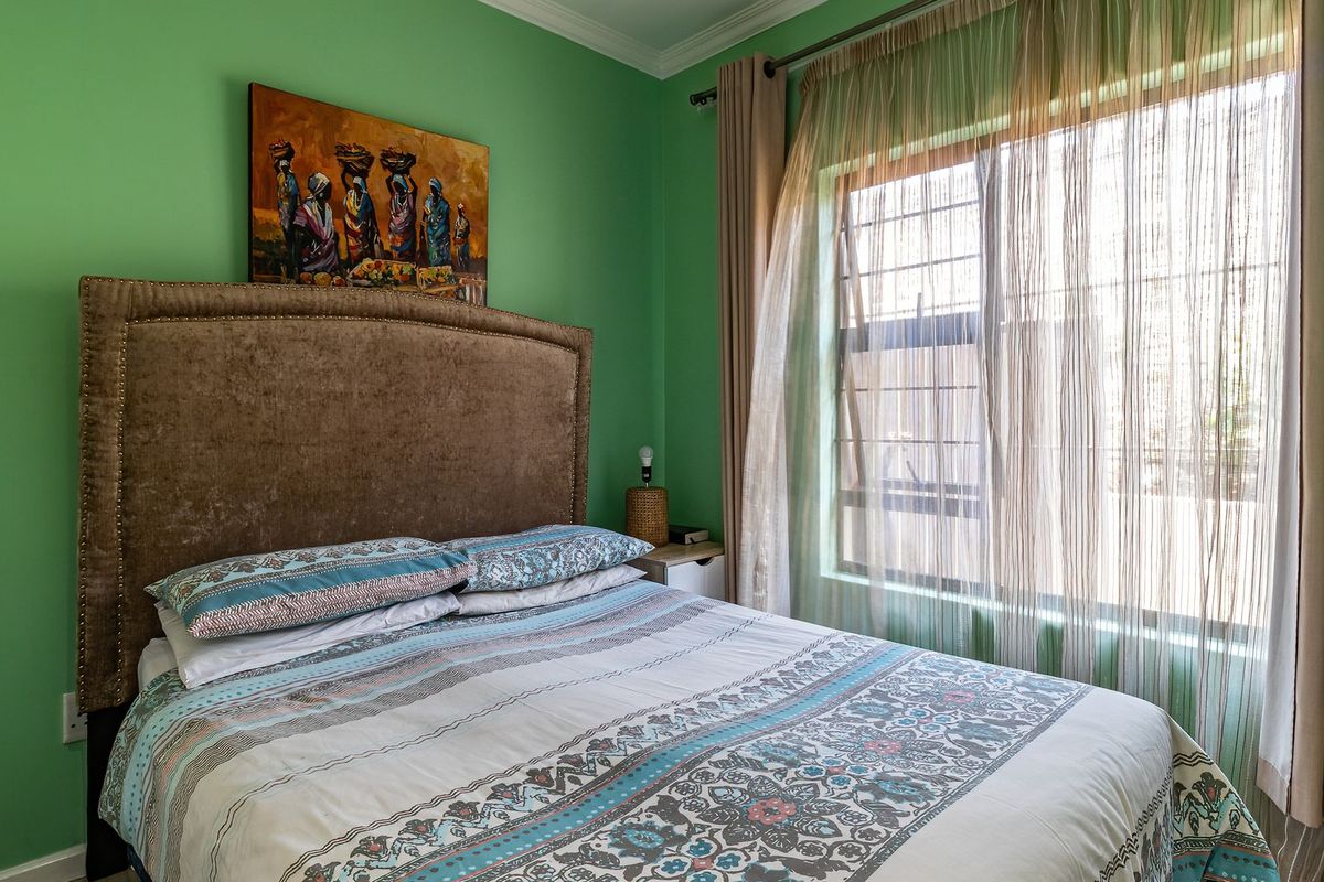 A bedroom featuring green walls, crown molding, and a window fitted with security bars, providing natural light.