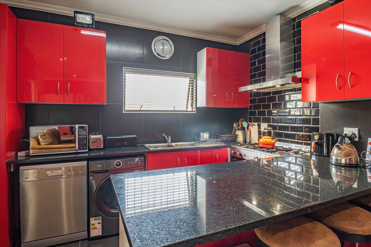 Modern kitchen featuring striking red high-gloss cabinetry, black granite countertops, a gas hob with stainless steel extractor, and integrated appliances.