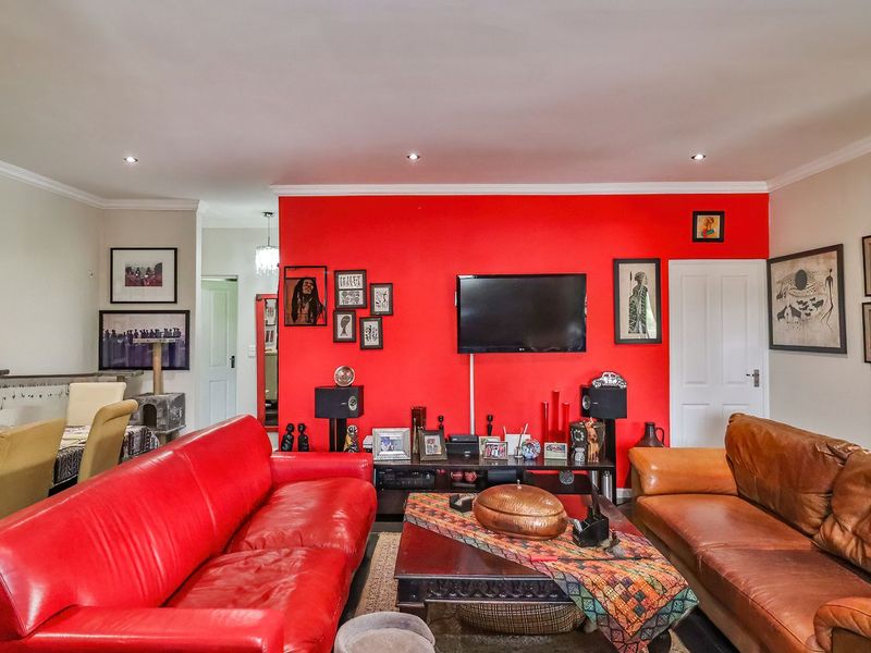 An open-plan living and dining area featuring recessed downlighting, coving, and a prominent red feature wall.