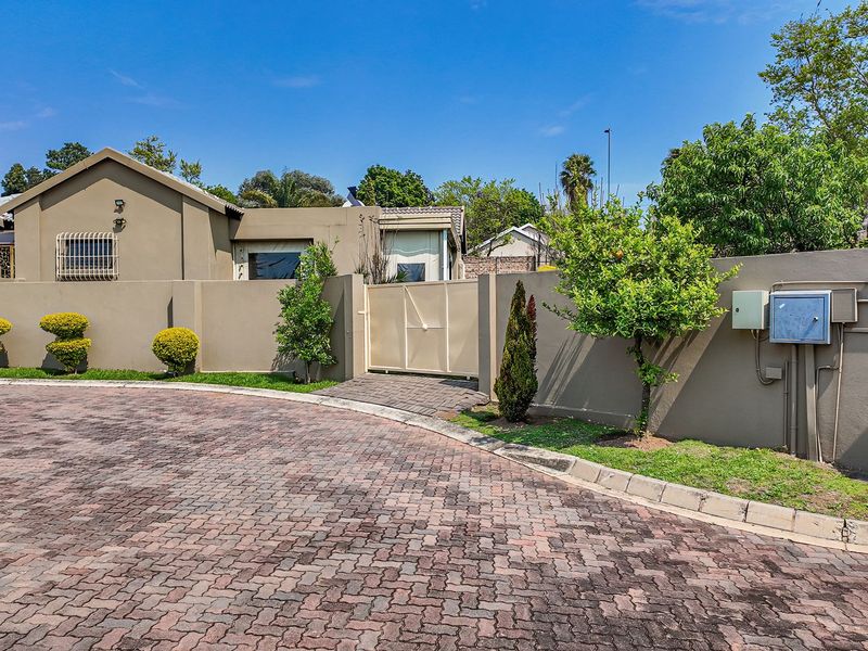 Front exterior view of the property featuring a paved driveway, secure boundary wall with pedestrian gate, and a single garage.