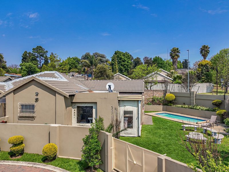 Aerial view of a residential property featuring a swimming pool, landscaped garden, paved driveway, and secure boundary walls.