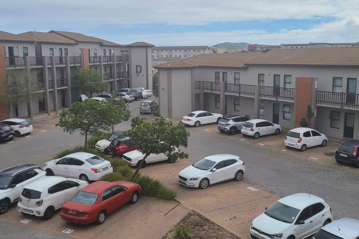 An elevated view of an apartment complex courtyard featuring paved parking bays and multi-story residential blocks with balconies.