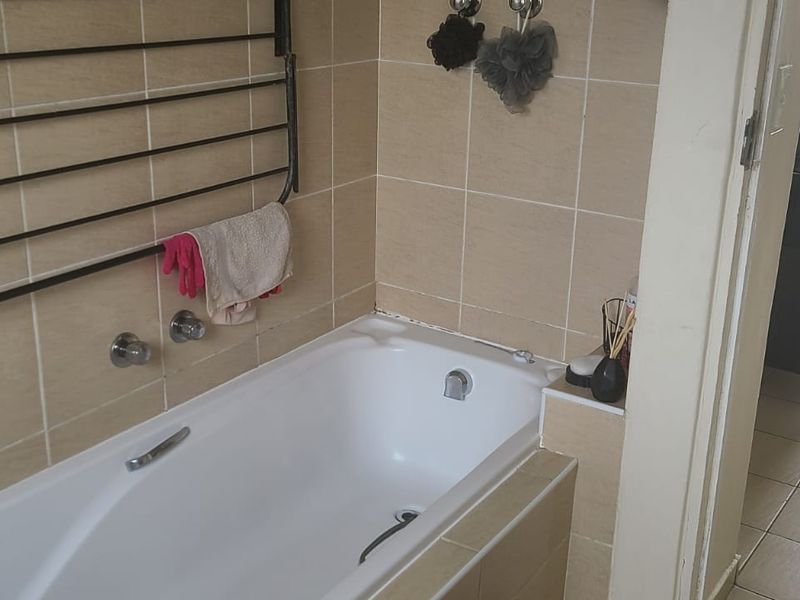 A functional bathroom featuring a built-in bathtub with wall-mounted mixer taps and neutral ceramic wall tiling.
