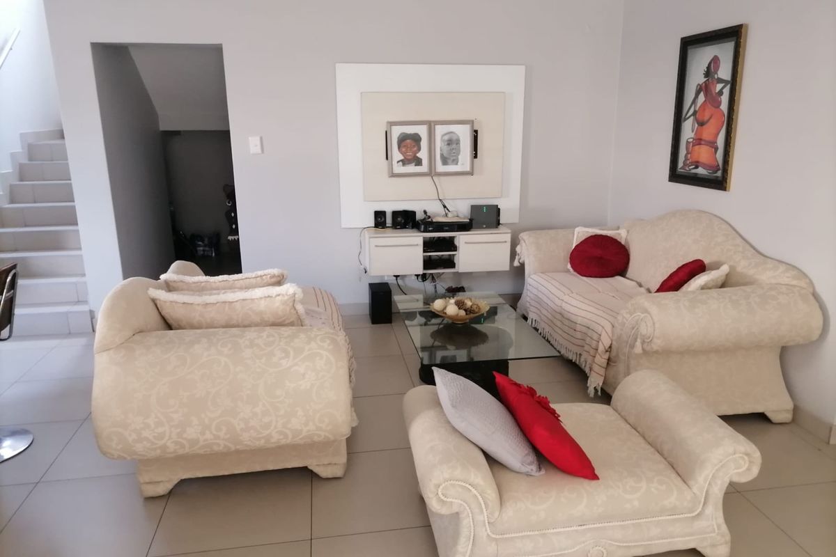 A comfortable living room featuring neutral tiled flooring, a wall-mounted media console, and an adjacent staircase leading to the upper level.