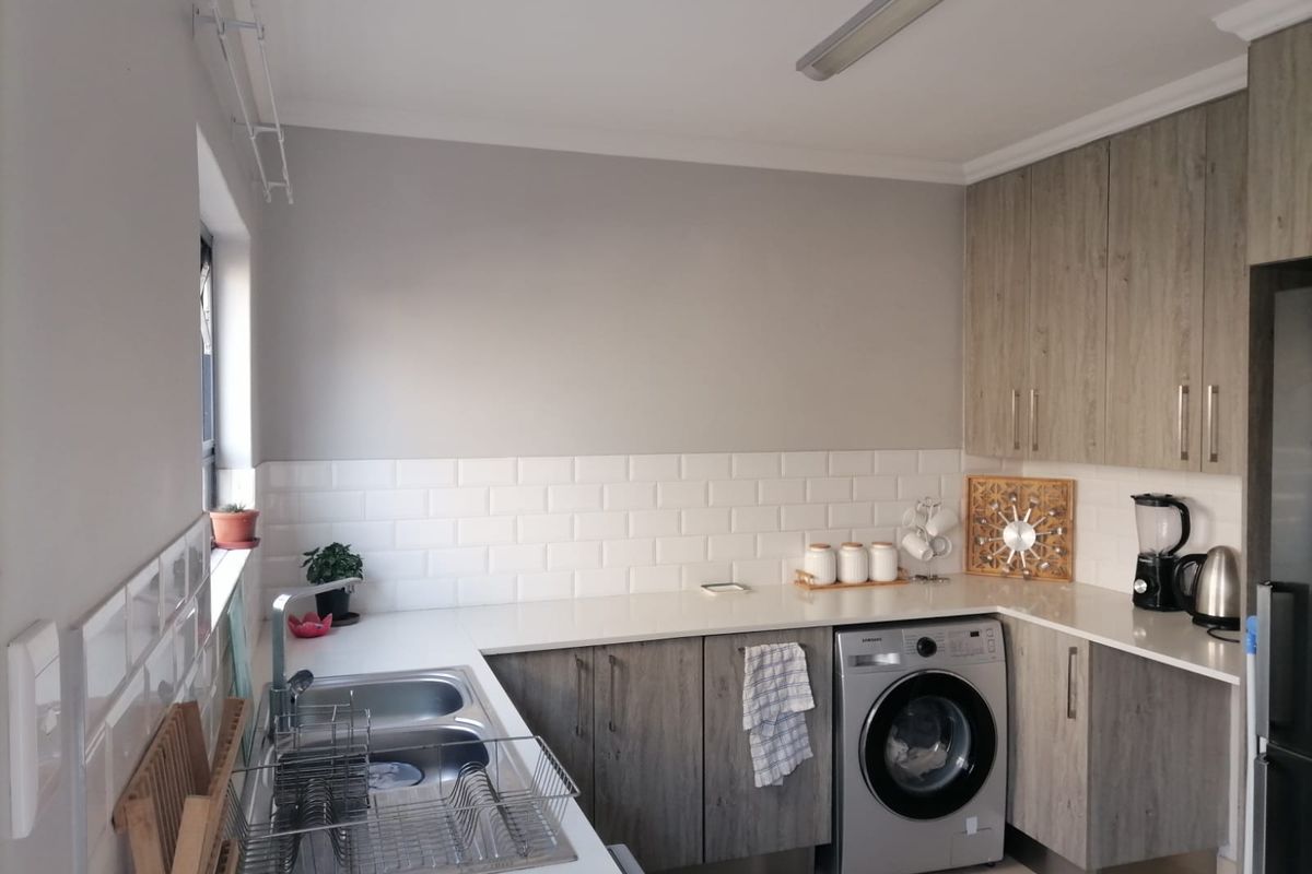 Modern kitchen featuring light wood-grain cabinetry, white quartz countertops, a classic subway tile backsplash, and integrated space for a washing machine.