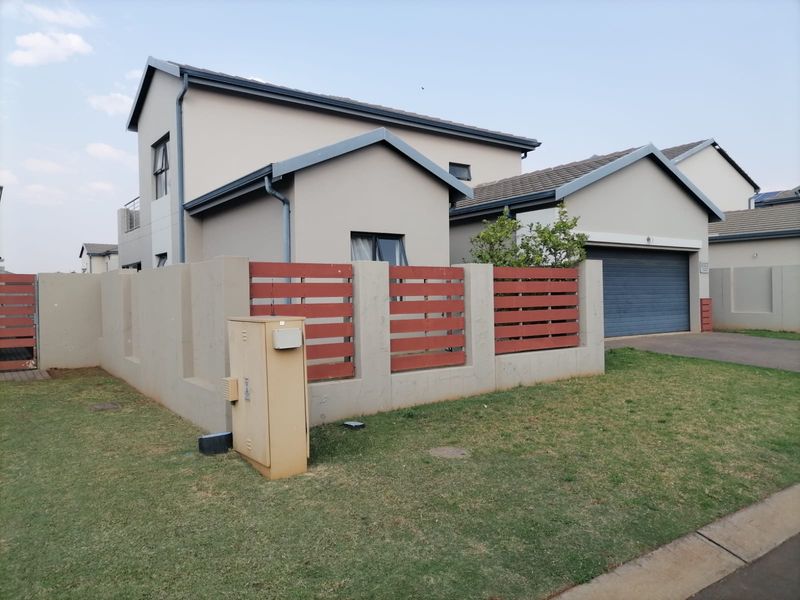 Front exterior view of a modern double-story house featuring a paved driveway, double garage, and a secure boundary wall with timber slat fencing.