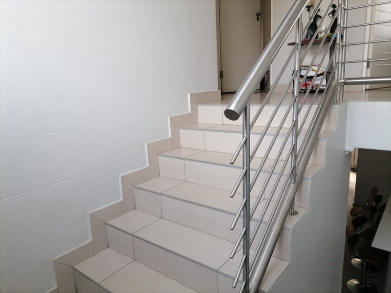 A clean, modern staircase featuring tiled steps and a contemporary stainless steel balustrade, providing access between levels.