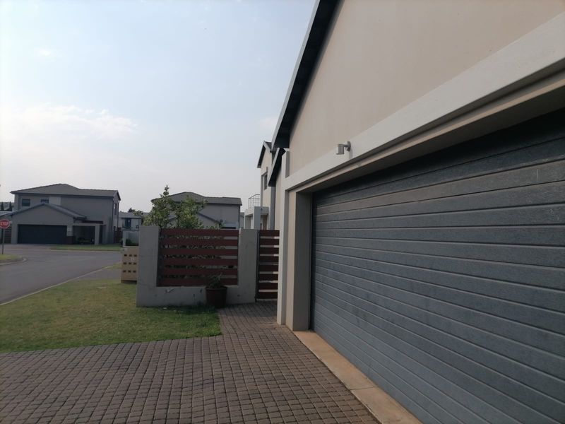 Front exterior view of the property featuring a paved driveway, a modern sectional garage door, and a secure boundary wall with a timber gate.