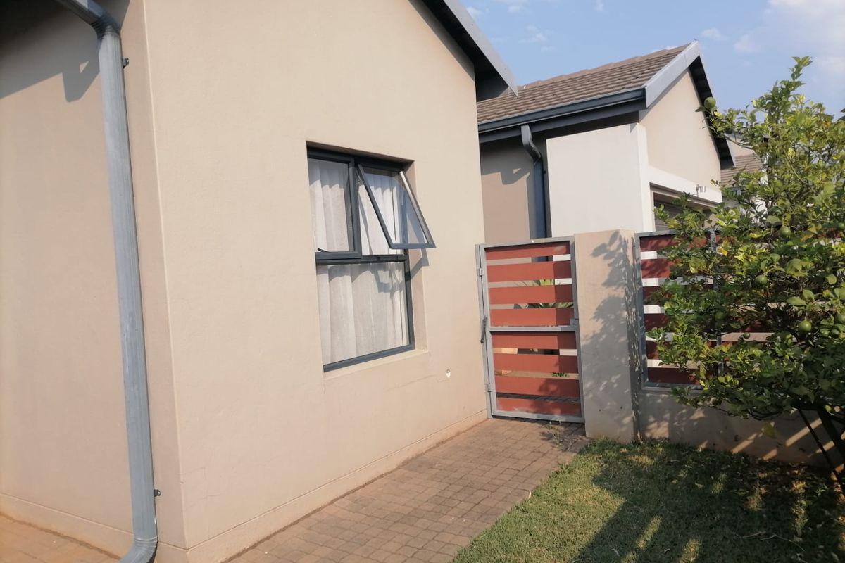 A view of the rear exterior featuring a paved walkway, aluminium window, and a timber slat gate leading to the side garden area.