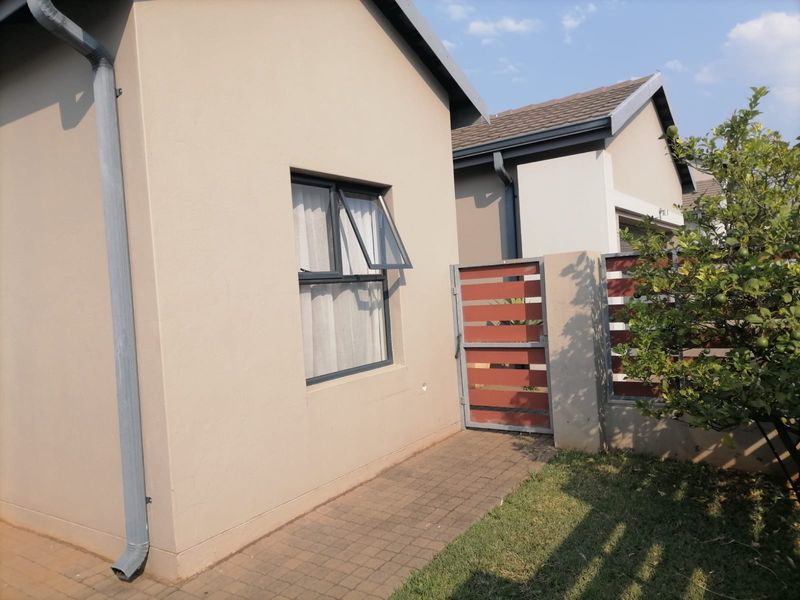 A view of the rear exterior featuring a paved walkway, aluminium window, and a timber slat gate leading to the side garden area.