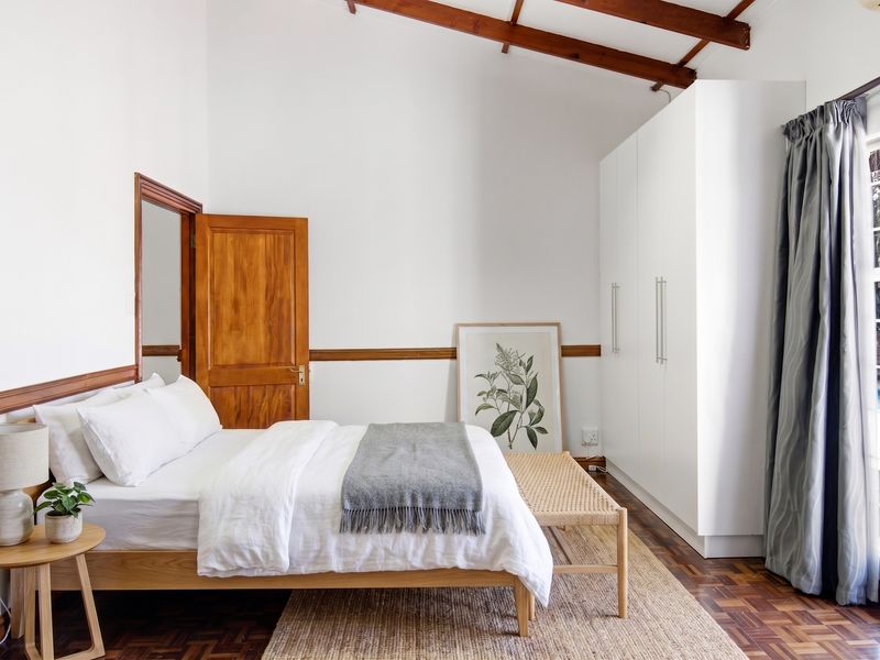 Bright bedroom featuring exposed timber ceiling beams, parquet flooring, built-in wardrobes, and a sliding glass door providing access to the pool area.