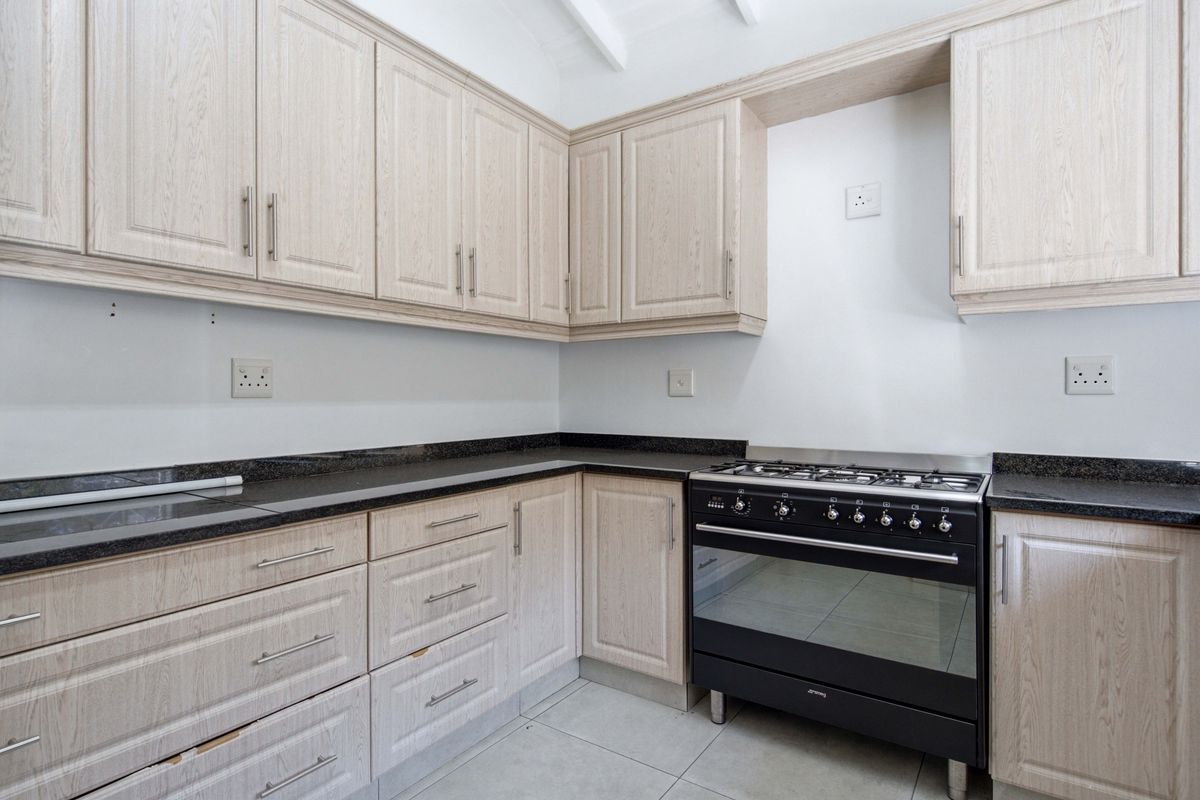 A functional kitchen featuring light wood-look cabinetry, dark granite countertops, and a freestanding gas stove, set against a neutral backdrop with tiled flooring.