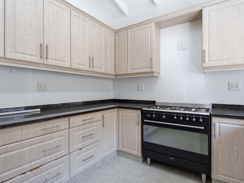 A functional kitchen featuring light wood-look cabinetry, dark granite countertops, and a freestanding gas stove, set against a neutral backdrop with tiled flooring.