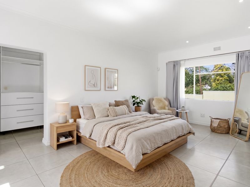 A bright and spacious bedroom featuring neutral tiled flooring, recessed lighting, and a convenient built-in wardrobe with integrated shelving and drawers.
