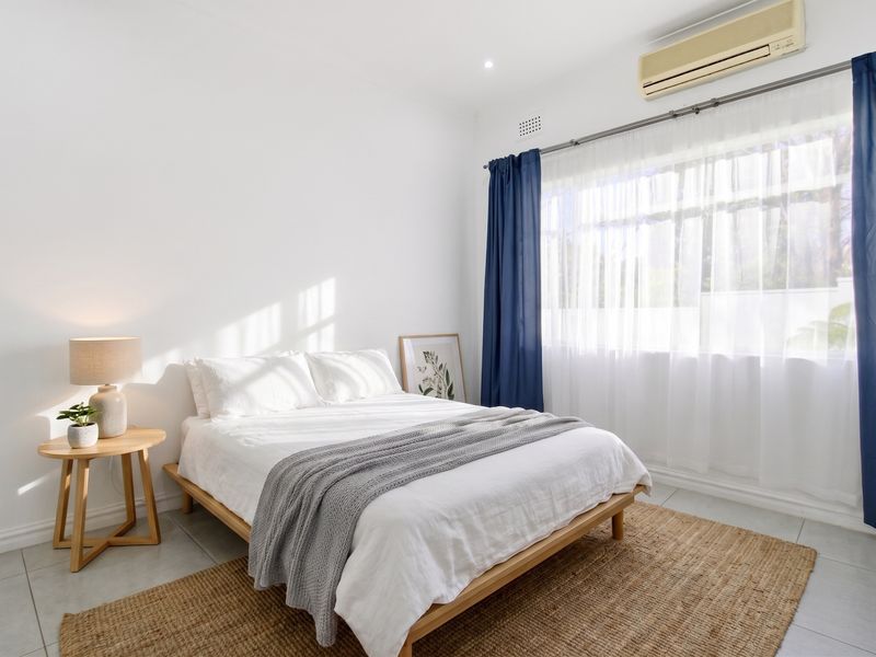 A bright and well-maintained bedroom featuring tiled flooring, a split-system air conditioner, and large windows with curtain fixtures.
