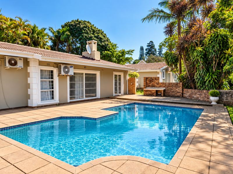 A well-maintained outdoor pool area featuring a tiled deck, built-in brick braai, and direct access to the home via sliding glass doors.