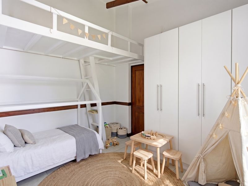 A bright bedroom featuring a built-in loft bed structure, ample white built-in wardrobes, and tiled flooring.